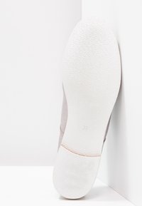 Chaussure à enfiler rose clair avec une tige en tissu texturé, une semelle en caoutchouc blanche et un contour lisse. La semelle présente un motif géométrique subtil.