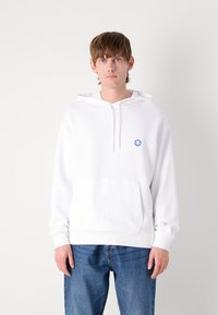 Felpa bianca con cappuccio e tasca frontale, presenta un piccolo logo blu a forma di sorriso sul petto, realizzata in un morbido tessuto misto cotone.
