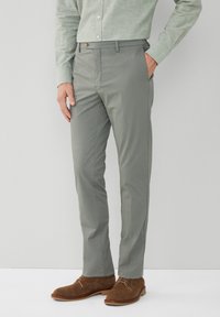 Lichtgrijze broek in een slim fit met een gladde textuur. Voorzien van een knoopsluiting en zijzakken. Gekleed met bruine suède schoenen.
