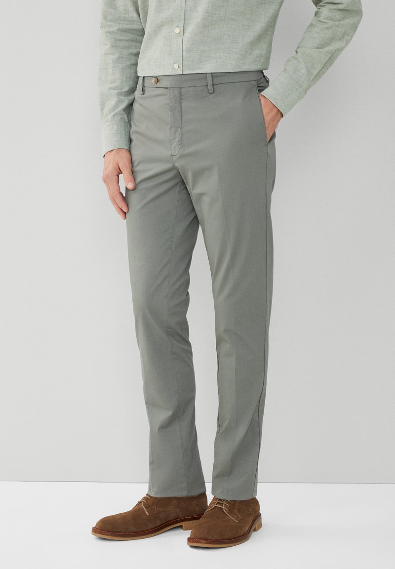 Lichtgrijze broek in een slim fit met een gladde textuur. Voorzien van een knoopsluiting en zijzakken. Gekleed met bruine suède schoenen.
