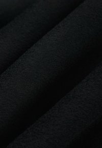 Czarna tkanina o miękkiej, aksamitnej fakturze. Materiał wydaje się gładki i lekko odblaskowy, ukazując zgięcia i głębię.