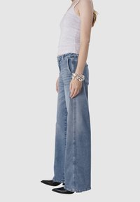 Lichtblauwe high-waisted wide-leg jeans met een rauwe zoom, gecombineerd met een grijze tanktop en zwarte puntige schoenen. Zilveren chunky armband om de pols.
