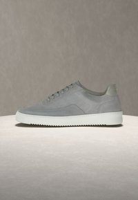 Γκρι sneaker από σουέντ με διάτρητες πλευρικές επιφάνειες, λευκή παχιά σόλα με ανάγλυφο πάτο και κλείσιμο με κορδόνια σε ουδέτερο φόντο.