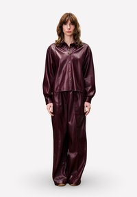 Bordeauxkleurig faux leren overhemd en bijpassende broek met wijde pijpen. Het overhemd heeft een kraag en knopen; de broek heeft zijzakken en een gladde afwerking.