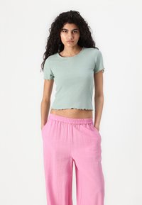 Top corto a coste verde chiaro con maniche corte a forma di scallop, abbinato a pantaloni rosa larghi con vita elastica. Tessuto morbido e vestibilità rilassata.