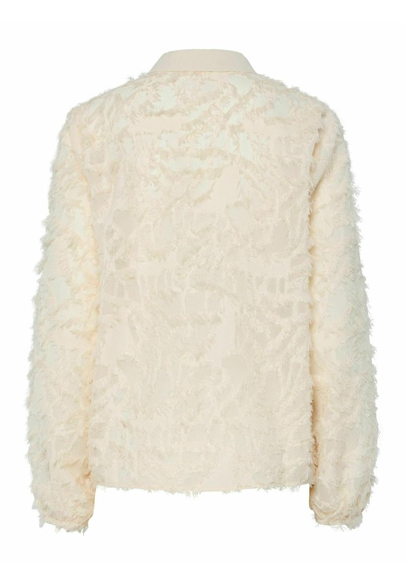 Cremefarbene Kunstfelljacke mit strukturierter Oberfläche, langen Ärmeln und klassischem Kragen; mit einem weichen, gewellten Muster durchzogen.