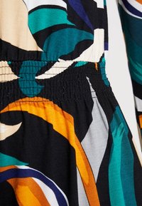 Wielokolorowa tkanina z wyrazistymi, abstrakcyjnymi wzorami liści w odcieniach zieleni, pomarańczy i beżu. Teksturowana czarna talia z elastycznym ściągaczem.