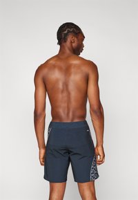 Men's swim shorts in dark navy with a textured waistband and patterned side panels. Features a fitted design and mid-thigh length.