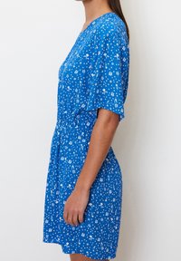 Kortärmad klänning i klarblått tyg med ett vitt blommönster, avslappnad passform och elastisk midja för ökad komfort.