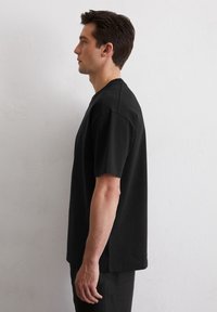 Zwarte korte mouwen t-shirt met een ontspannen pasvorm, ronde hals en subtiele details aan de zijnaad, gemaakt van zachte katoenstof.