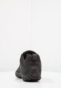 Scarpa nera da esterno con tomaia in rete testurizzata, colletto imbottito e suola in gomma. Presenta un tallone di supporto e un dettaglio logo sul retro.