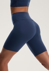 Sötétkék, magas derekú kerékpáros rövidnadrág rugalmas anyagból, sima textúrával és térd hosszúságú dizájnnal, látható minták nélkül.