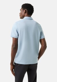 Lichtblauw poloshirt met korte mouwen, klassieke kraag en een gladde textuur. Draagt bij een donkere broek, met een ontspannen pasvorm en eenvoudig ontwerp.