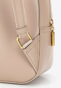 Borsa in pelle beige con una superficie liscia, dettagli in hardware dorato e doppie cuciture. Presenta un'etichetta del marchio incisa attaccata alla cerniera.