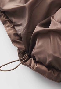 Tissu brun texturé avec un bord froncé et un cordon de serrage. Douceur notable et léger brillant, convient pour une utilisation extérieure ou protectrice.