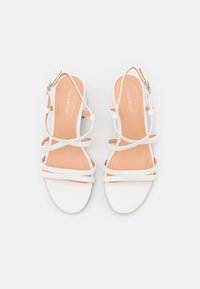 Vita remjande sandaler med platt sula, justerbart vristband och en slät matt yta. Innersulan har en mjuk beige färg.