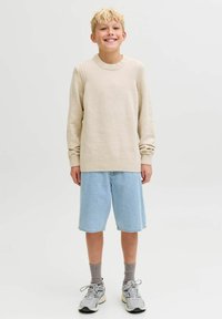 Šviesiai smėlinės spalvos megztinis su raukšlėtu apykaklėje, derinamas su šviesiai mėlynomis džinsinėmis šortais. Nešiojamas su pilkomis kojinėmis ir pilkais sportbačiais.