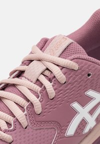 Pink athletic shoe featuring a textured synthetic upper, mesh collar, and fabric laces. Includes a white logo and patterned accents.