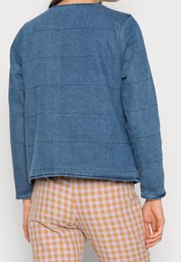 Jeanjacka i blått med kviltade horisontella ränder, rund halsringning, långa ärmar och rå fåll. Avslappnad passform med texturerad yta.