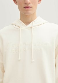 Biała bluza z kapturem, wykonana z miękkiego materiału, z wytłoczonym logiem i napisem "Established 2007 Denim Tom Tailor" na piersi. Kaptur ze sznurkiem.