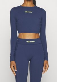 Top corto de manga larga en color navy y leggings de alta cintura hechos de material elástico, con un logo "ellesse" en verde claro en ambas prendas.