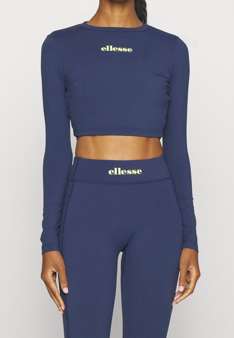 Top corto de manga larga en color navy y leggings de alta cintura hechos de material elástico, con un logo "ellesse" en verde claro en ambas prendas.