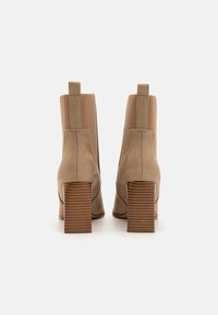Bottines en suède beige doux avec un bout carré. Présentent des panneaux élastiques sur les côtés et un talon bloc en bois à motif rayé.