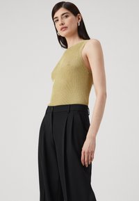Χρυσό ριμπ αμάνικο τοπ, εφαρμοστό σχήμα, με κιτρινωπές αποχρώσεις; σε συνδυασμό με ψηλόμεσα μαύρα παντελόνια, με πλισέ σχέδιο.