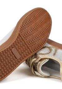 Bílé síťované tenisky se zlatými akcenty. Hnědá gumová podrážka s texturovaným gripem. Systém šněrování a logo viditelné na boku.