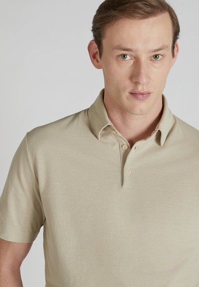 Beżowa koszulka polo z krótkim rękawem z teksturowanej tkaniny, z klasycznym kołnierzykiem, z dwoma guzikami na listwie i luźnym krojem.