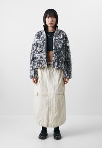 Fuzzy black-and-white patterned zip-up jacket, paired with a cream-colored long skirt featuring pockets and elastic hem, worn with dark sneakers.