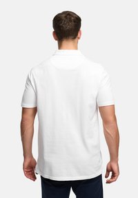 Hvid poloshirt med korte ærmer, lavet af glat stof. Har en standardkrave og en lige kant, der viser en afslappet pasform på en models ryg.