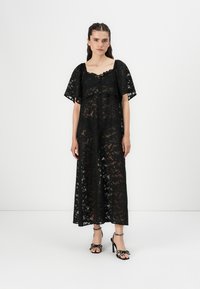 Black lace maxi dress with short sleeves, floral pattern, scoop neckline, and button details. Paired with black heeled sandals.