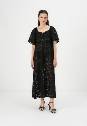 Black lace maxi dress with short sleeves, floral pattern, scoop neckline, and button details. Paired with black heeled sandals.
