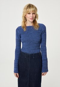 Blauw, gestructureerd gebreid shirt met lange mouwen en een vierkante halslijn, gecombineerd met een donkere spijkerrok met verticale naden en een aansluitende silhoutte.