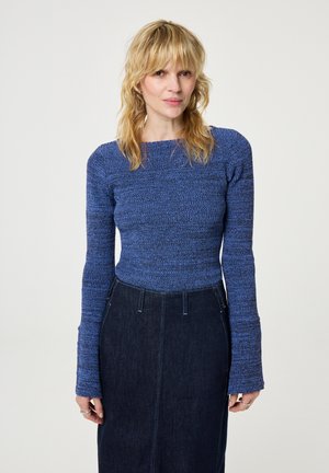 Blauw, gestructureerd gebreid shirt met lange mouwen en een vierkante halslijn, gecombineerd met een donkere spijkerrok met verticale naden en een aansluitende silhoutte.