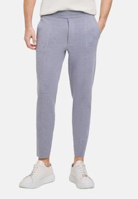Graue Jogginghose mit schmalem Schnitt, aus weichem Stoff, mit Seitentaschen und genähten Details, kombiniert mit weißen Sneakern.
