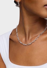 Collana in argento con anelli allungati interconnessi. Texture liscia e finitura lucida. Indossata con un capo bianco.