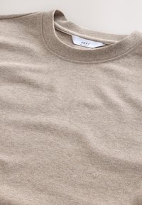 Beige T-shirt met ronde hals gemaakt van zacht stof met een gestructureerd oppervlak, een ontspannen pasvorm en een label met de tekst "NEXT RELAXED FIT".