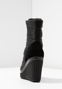 Černé kotníkové boty na klínku s prošívaným nylonovým svrškem a semišovým akcentem. Mají texturovaný klínek a zadní poutko pro snadné obouvání.