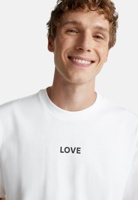 Camiseta de algodón blanca con un estampado negro de "LOVE" en el frente, cuello redondo y mangas cortas, textura suave.