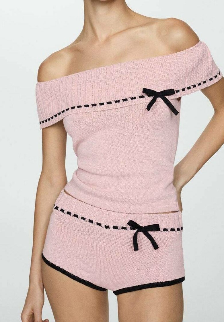 Růžový pletený top s odhalenými rameny, černým lemováním a mašličkovými detaily, doplněný o odpovídající šortky se stejným lemováním a detaily.