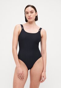 Maillot de bain une pièce noir avec un design texturé, décolleté carré et larges bretelles ornées de détails en métal. Silhouette lisse et ajustée.