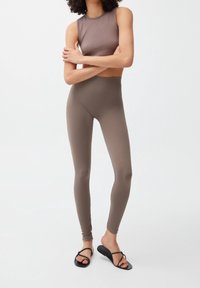 Bruin geribbeld crop top gecombineerd met hoog-waisted bijpassende leggings, die een strakke pasvorm en een gladde textuur tonen. Zwarte flip-flops maken de look compleet.