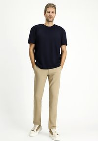 T-shirt blu navy a maniche corte, pantaloni beige slim-fit e sneakers bianche. L'outfit presenta un design classico con una vestibilità rilassata.