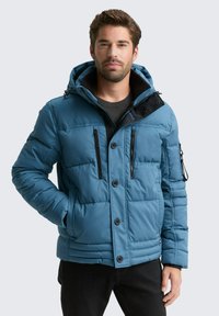 Blaue gepolsterte Jacke mit Kapuze, die schwarze Akzente, mehrere Rei�ßverschlusstaschen und einen Knopfverschluss aufweist. Der Stoff hat eine glatte Textur.