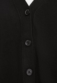 Cárdigan negro de punto con diseño de escote en V y cuatro botones redondos negros en la parte delantera. Textura suave con detalles acanalados a lo largo de los bordes.