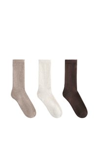 Drie geribbelde crew-sokken in beige, wit en donkerbruin, naast elkaar weergegeven op een witte achtergrond.