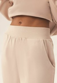 Jasno beżowe dresy wykonane z miękkiego materiału, z prążkowanym pasem, delikatnymi fałdami i bocznymi kieszeniami dla dodatkowej funkcjonalności.