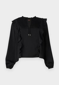 Blouse noire à manches longues avec des accents à volants sur le devant et les épaules. Dispose d'un col à cordon de serrage et d'un tissu texturé. Design court.